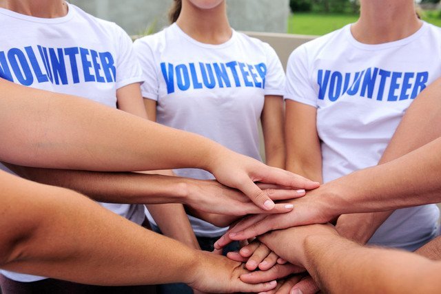 Ladies in a circle, clasping hands, wearing white t-shirts with the logo VOLUNTEER in blue