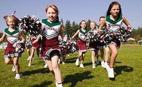 Little girls wearing cheerleader outfits, running in a field 